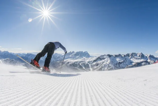 a skier sets off on perfect groomed piste, a sun shining above