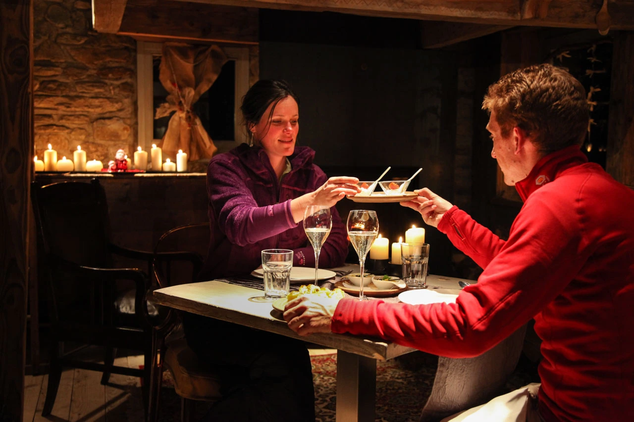 two share a romantic dinner in a low-lit chalet