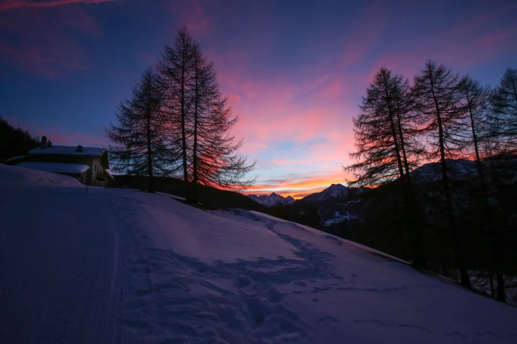 a colourful sunset over high mountain peaks in the distance, a stone chalet in the foreground