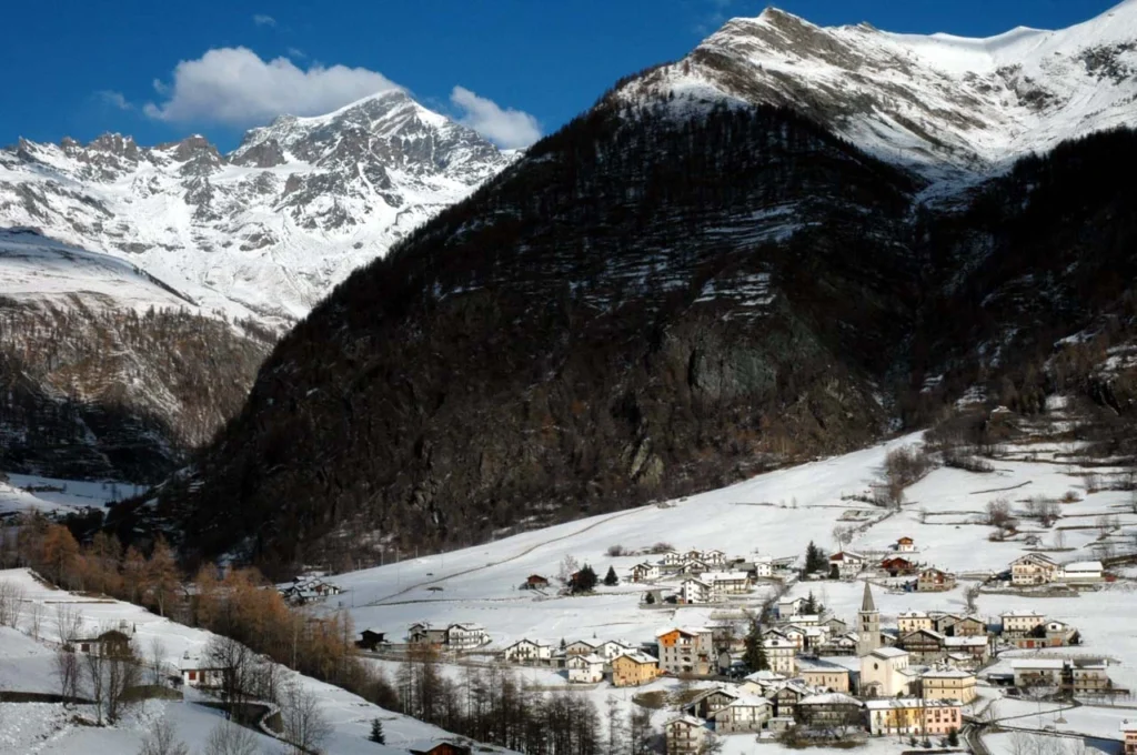 a snow-covered mountain hamlet is photographed from a hill above