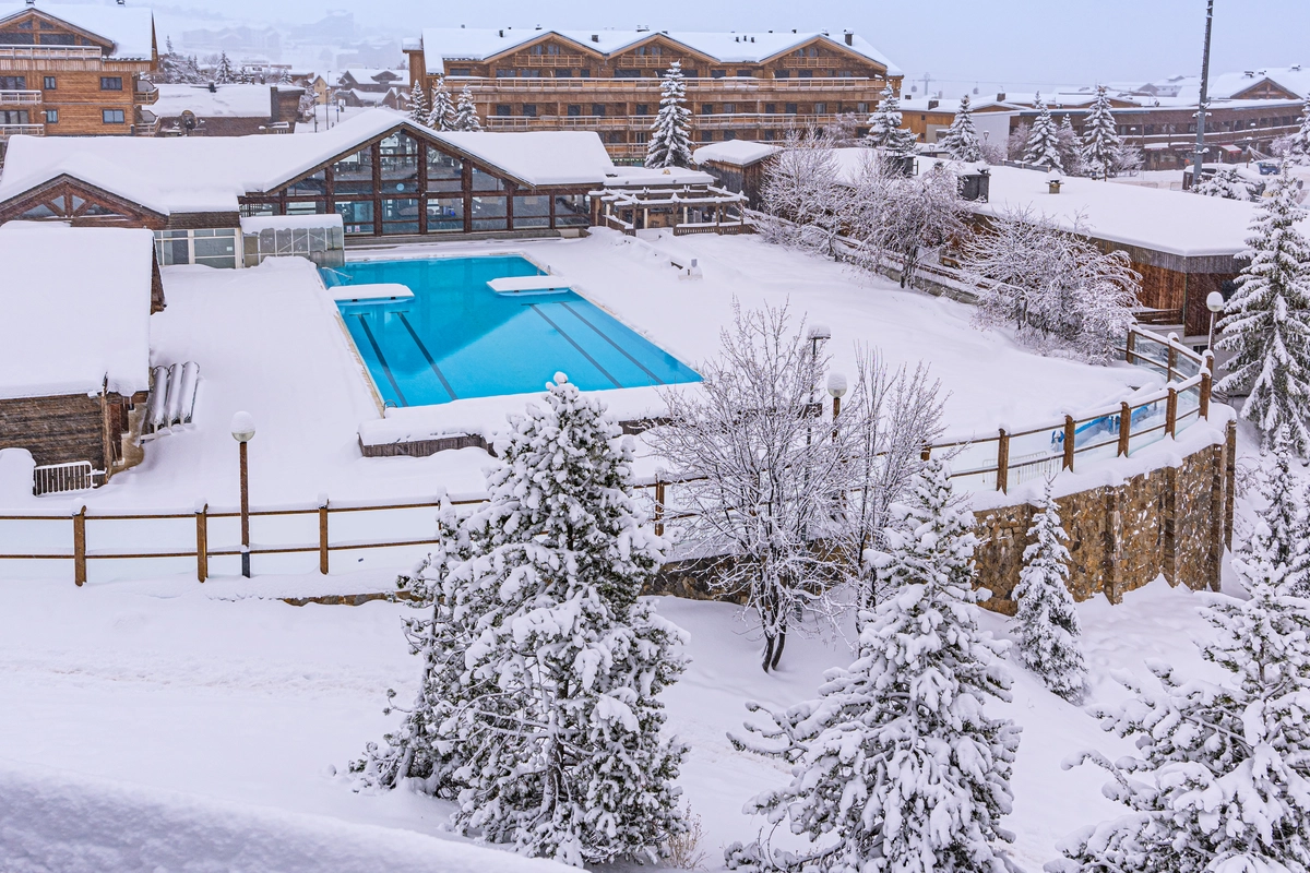 an outdoor pool surrounded by snow and the alpine village of Alpe d'Huez