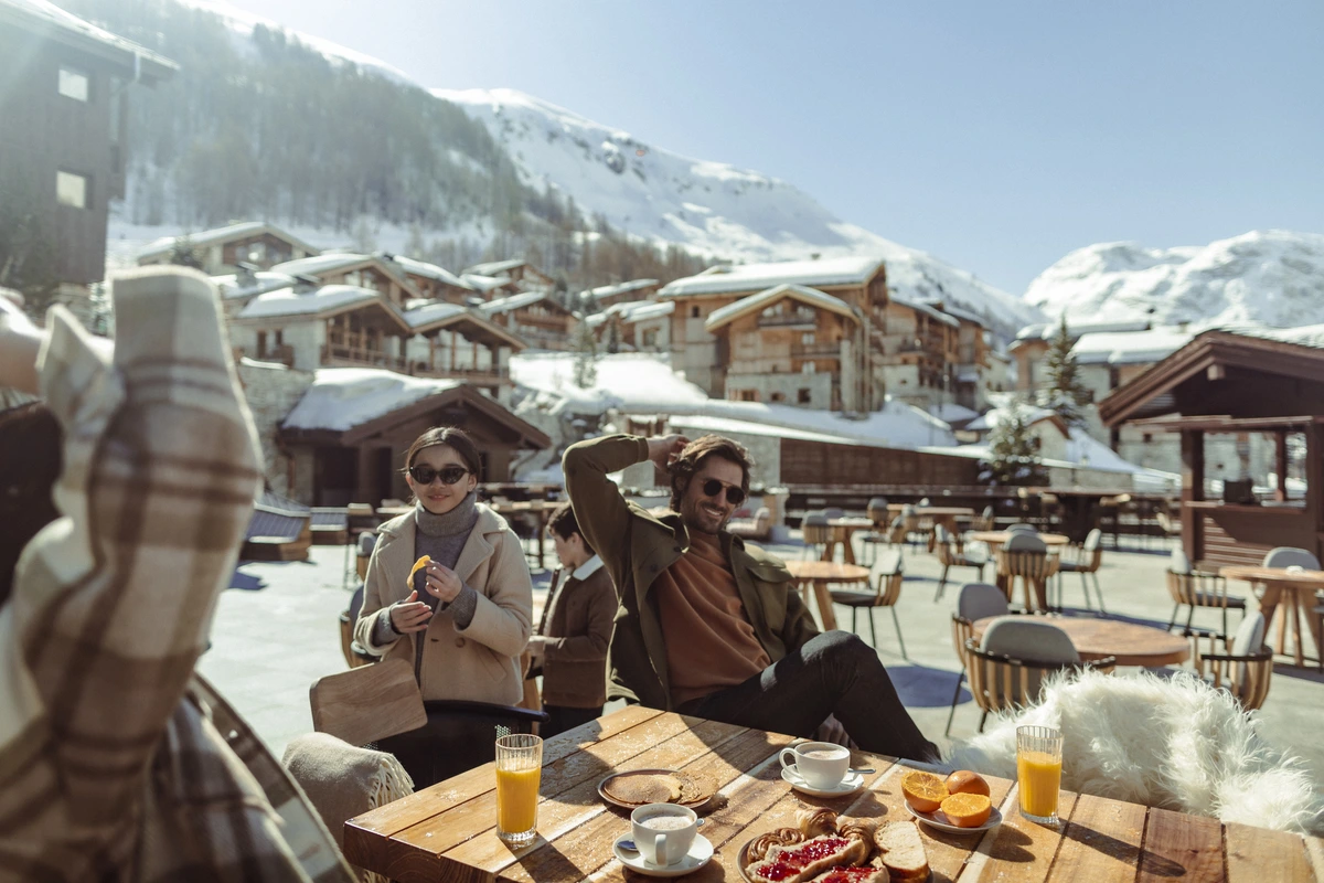 a chilled après ski scene with friends sitting round a slope-side table of drinks under the sun