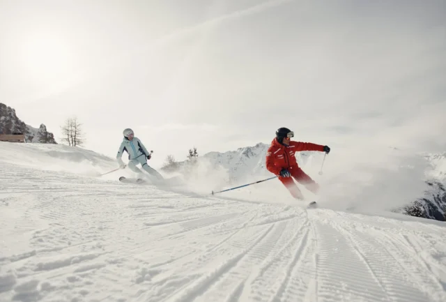 two skiers - one an instructor - carve side by side down a slope