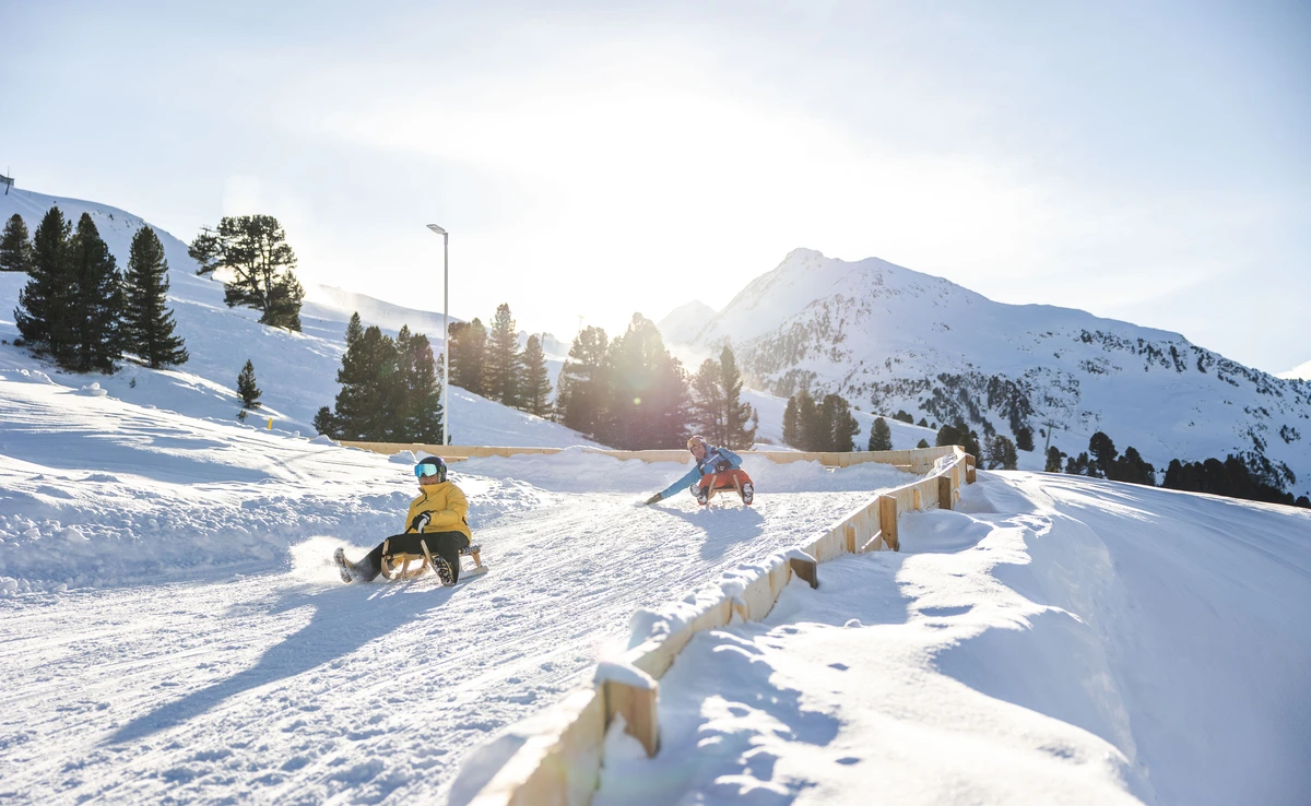 two adults sled down a special track in a snowy landscape