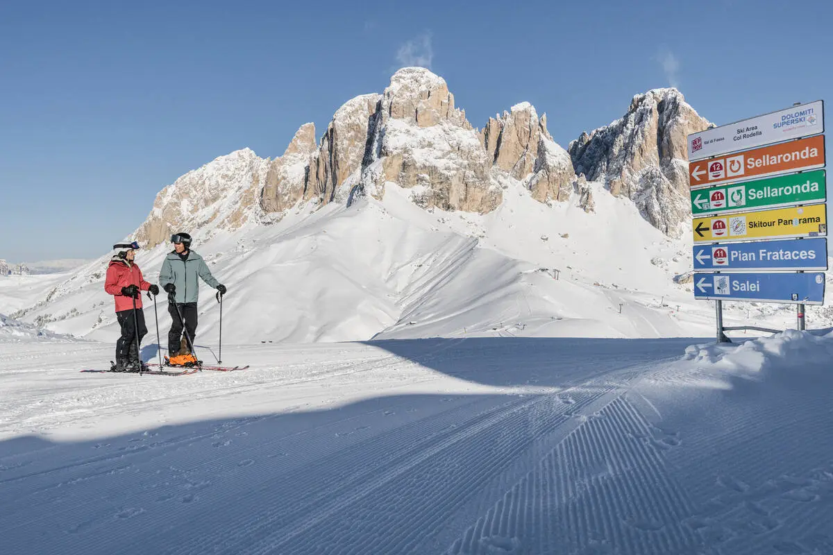 two skiers stand on mountain near piste signs, deciding their route