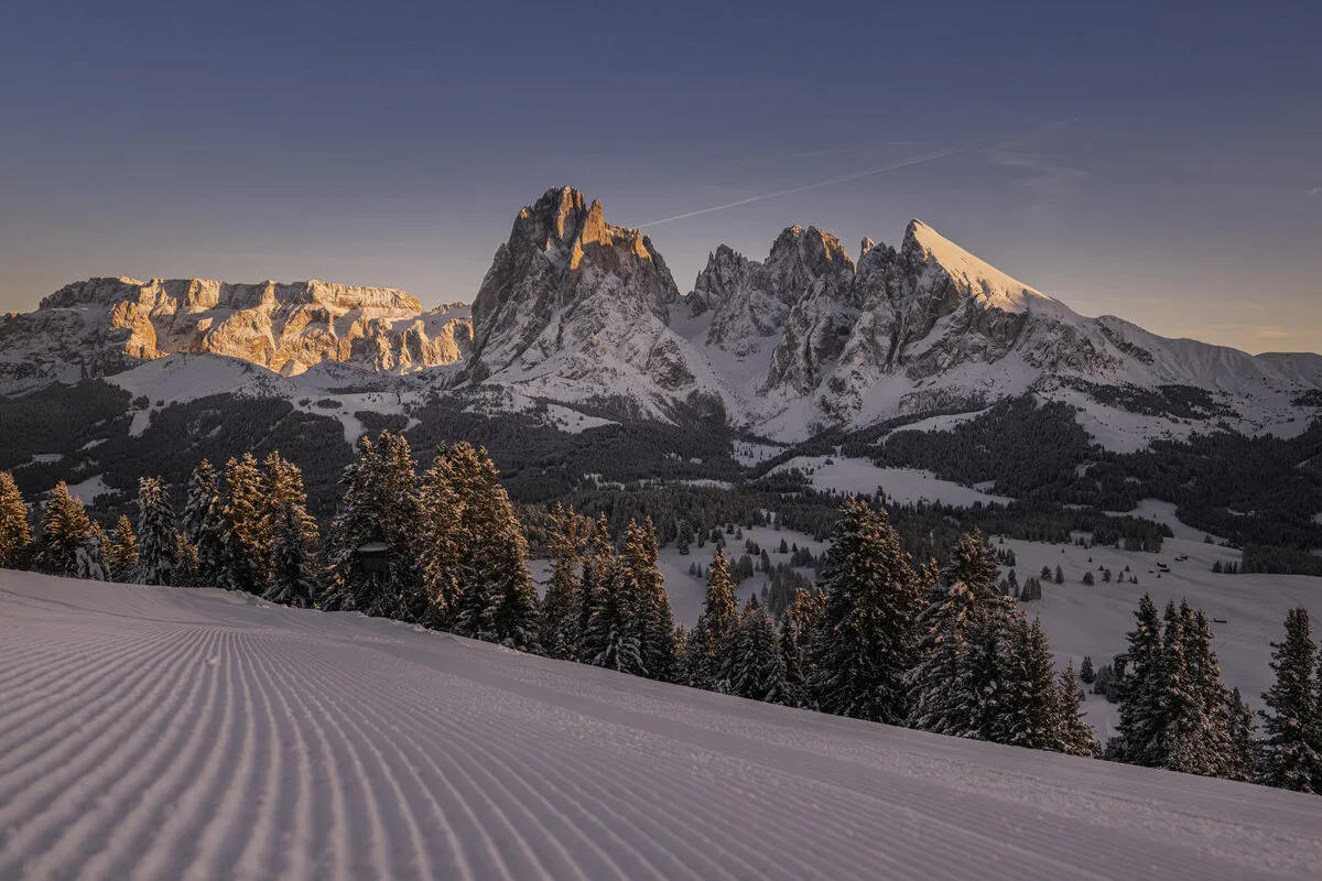 corduroy piste and jagged snowy mountains at sunset