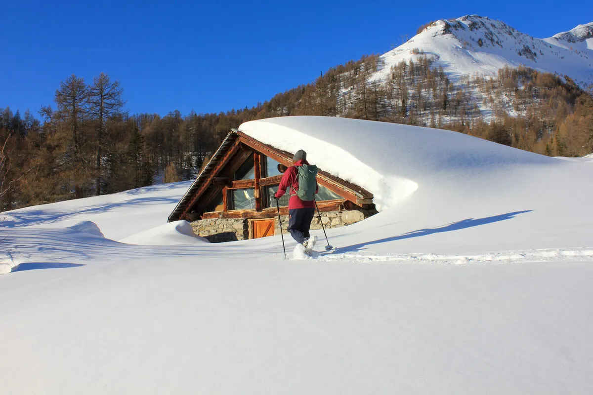 a snowshoer walks in front of a snow-covered chalet