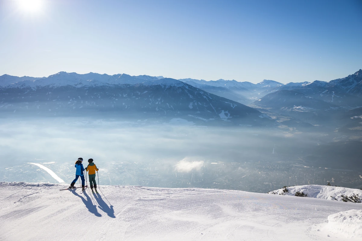 two skiers stand atop a hill looking out over a valley view. Nordkette © Innsbruck Tourismus / Eye5 - Jonas Schwarzwälder