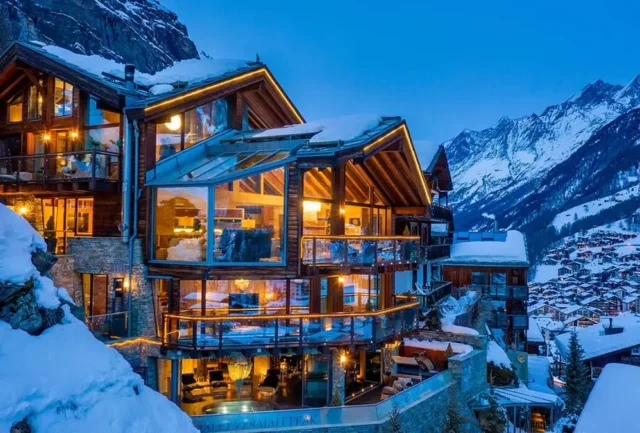 large glass and wooden chalet under snow at night